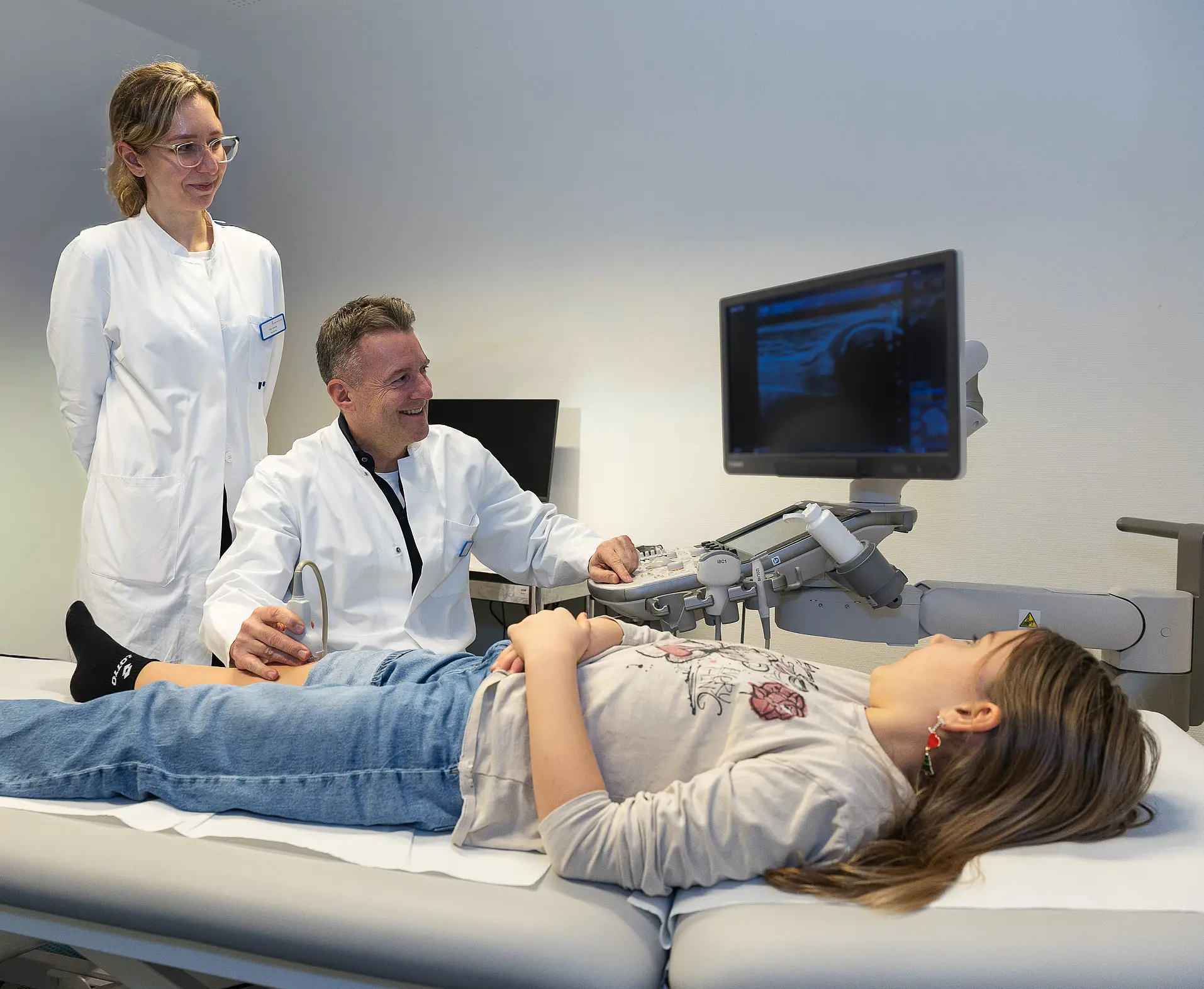 Ein Kind liegt entspannt auf einer Untersuchungsliege, während ein Arzt eine Ultraschalluntersuchung durchführt.
