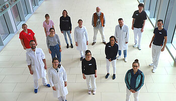 Mehrere Mitarbeitende der Kinder- und Jugendrheumatologie stehen in einem hellen Klinikflur und blicken zur Kamera.