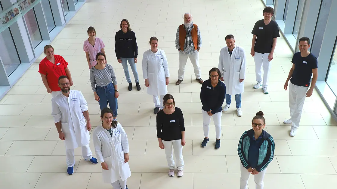 Mehrere Mitarbeitende der Kinder- und Jugendrheumatologie stehen in einem hellen Klinikflur und blicken zur Kamera.
