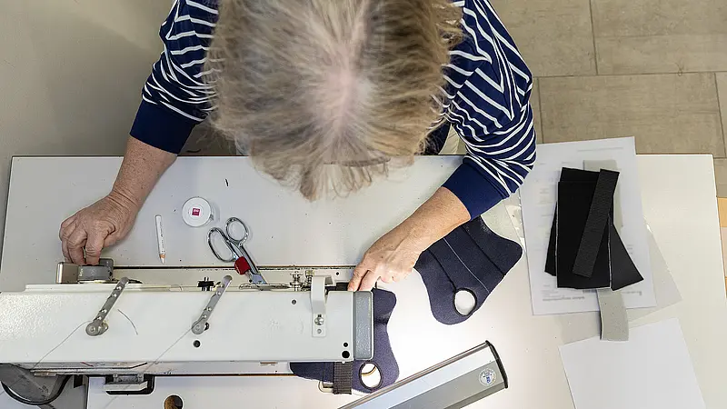 Hände einer Mitarbeiterin positionieren Stoff exakt an der Nadel einer Industrienähmaschine.