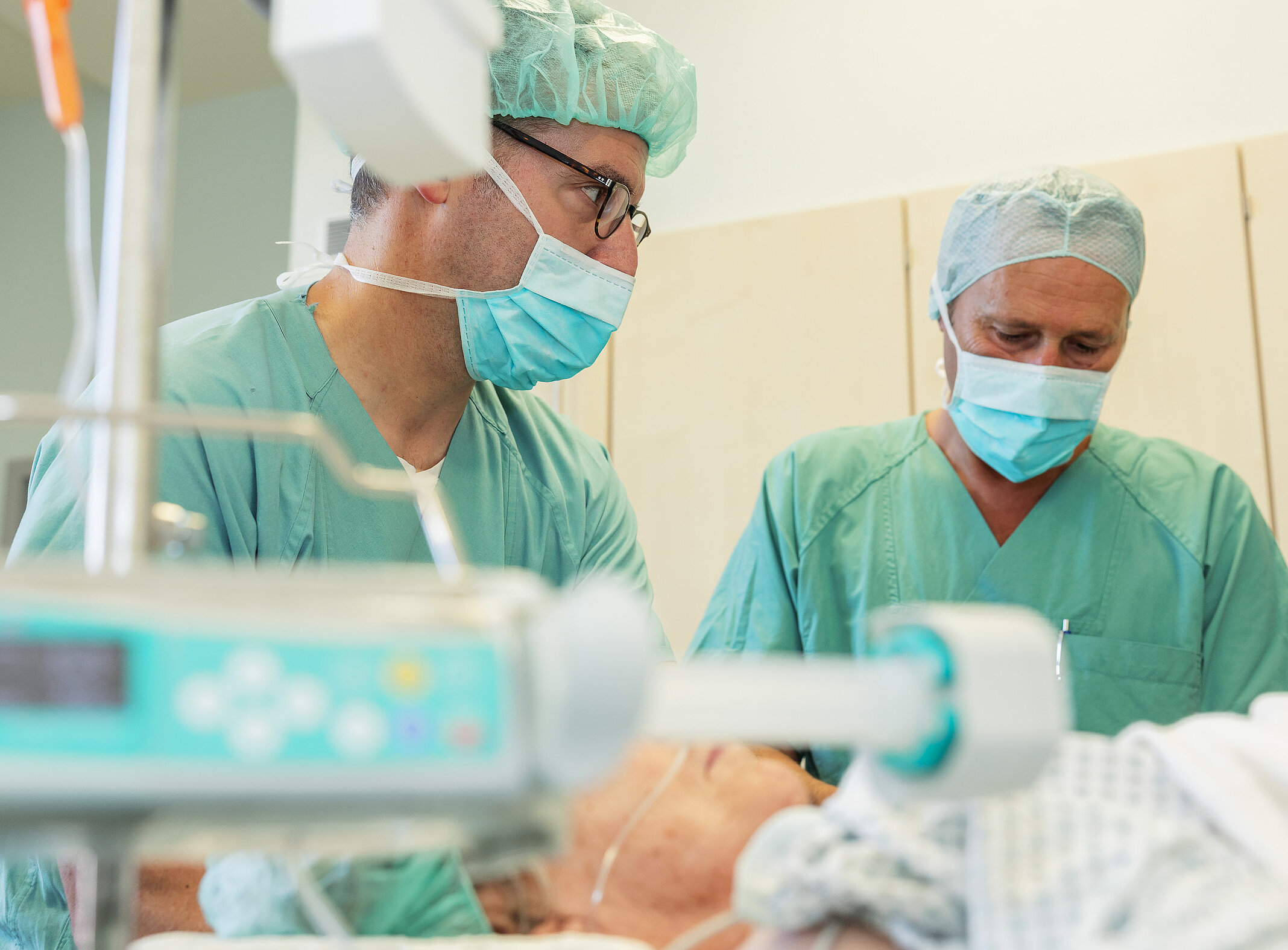 Chefarzt Dr. med. Matthias Boschin und ein weiterer Mitarbeiter in OP-Kleidung stehen an einem medizinischen Gerät und stimmen Abläufe ab.