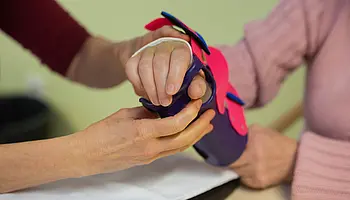 Feinjustierung einer Handorthese für eine sichere und funktionelle Unterstützung. ALT-Text: Nahaufnahme von Händen, die eine Handorthese mit Riemen und kleinen Verschlüssen an einer Hand einstellen.