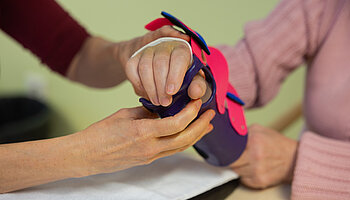 Feinjustierung einer Handorthese für eine sichere und funktionelle Unterstützung. ALT-Text: Nahaufnahme von Händen, die eine Handorthese mit Riemen und kleinen Verschlüssen an einer Hand einstellen.