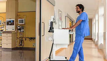 Mitarbeiter schiebt einen mobilen Computerwagen durch den Flur der Intensivobservation.