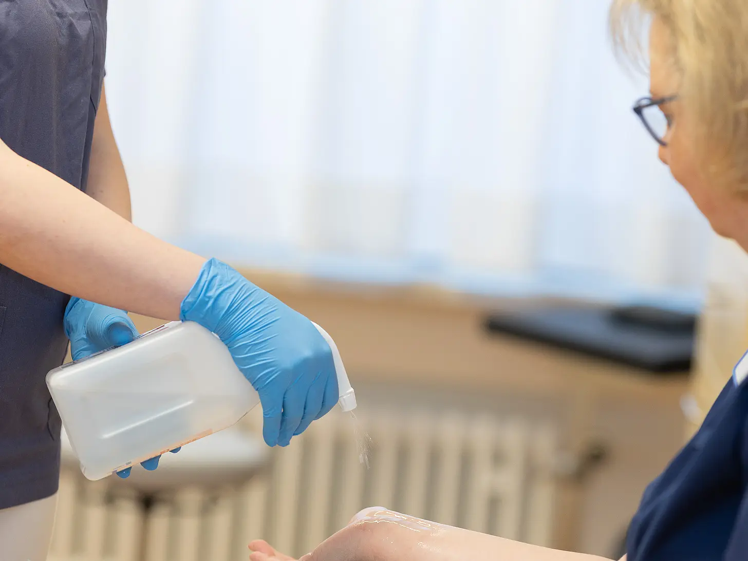 Eine Medizinische Fachangestellte sprüht einer Patientin Desinfektionsm