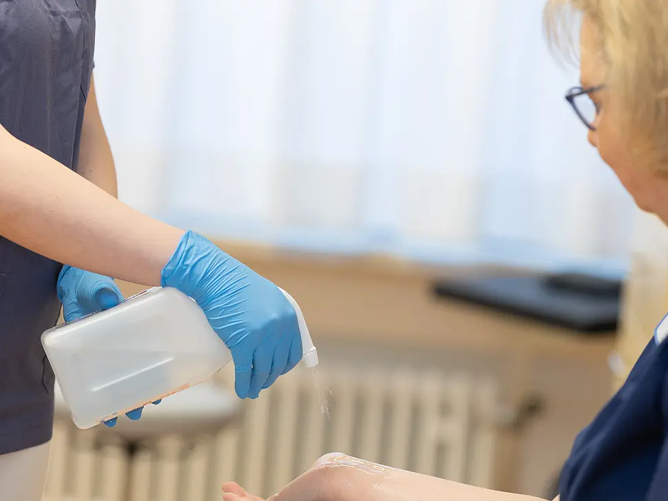 Eine Medizinische Fachangestellte sprüht einer Patientin Desinfektionsm