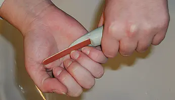 Eine Person hält eine Nagelfeile mit verdicktem, ergonomischem Griff; die vergrößerte Griffstärke ermöglicht eine bessere Kraftverteilung und entlastet Finger- und Handgelenke bei der Anwendung.