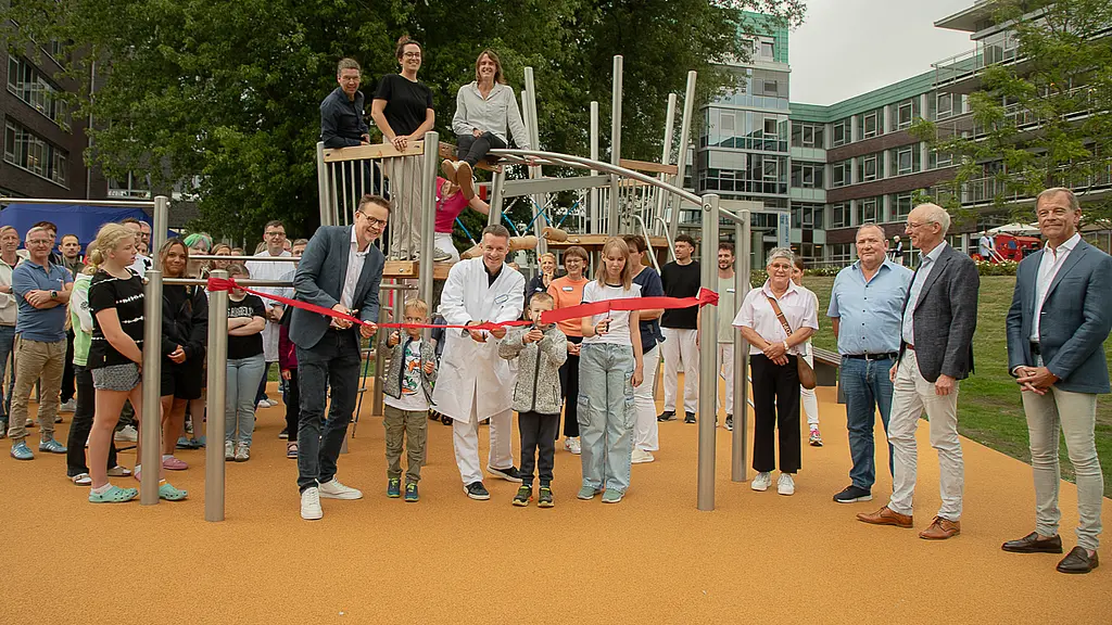 Das rote Band schnitten Kinder und Vertreter des St. Josef-Stifts symbolisch durch: Damit wurde der therapiegerechte Spielplatz Ende August 2028 offiziell eröffnet. Viele ältere und junge Menschen stehen auf einem neuen Spielplatz, in der Mitte ein Arzt im weißen Kittel, der symbolisch ein rotes Band mit einer Schere durchschneidet.