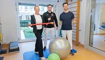 Eine Gruppe von Therapeutinnen und Therapeuten, die verschiedene Trainingsmittel in den Händen halten.