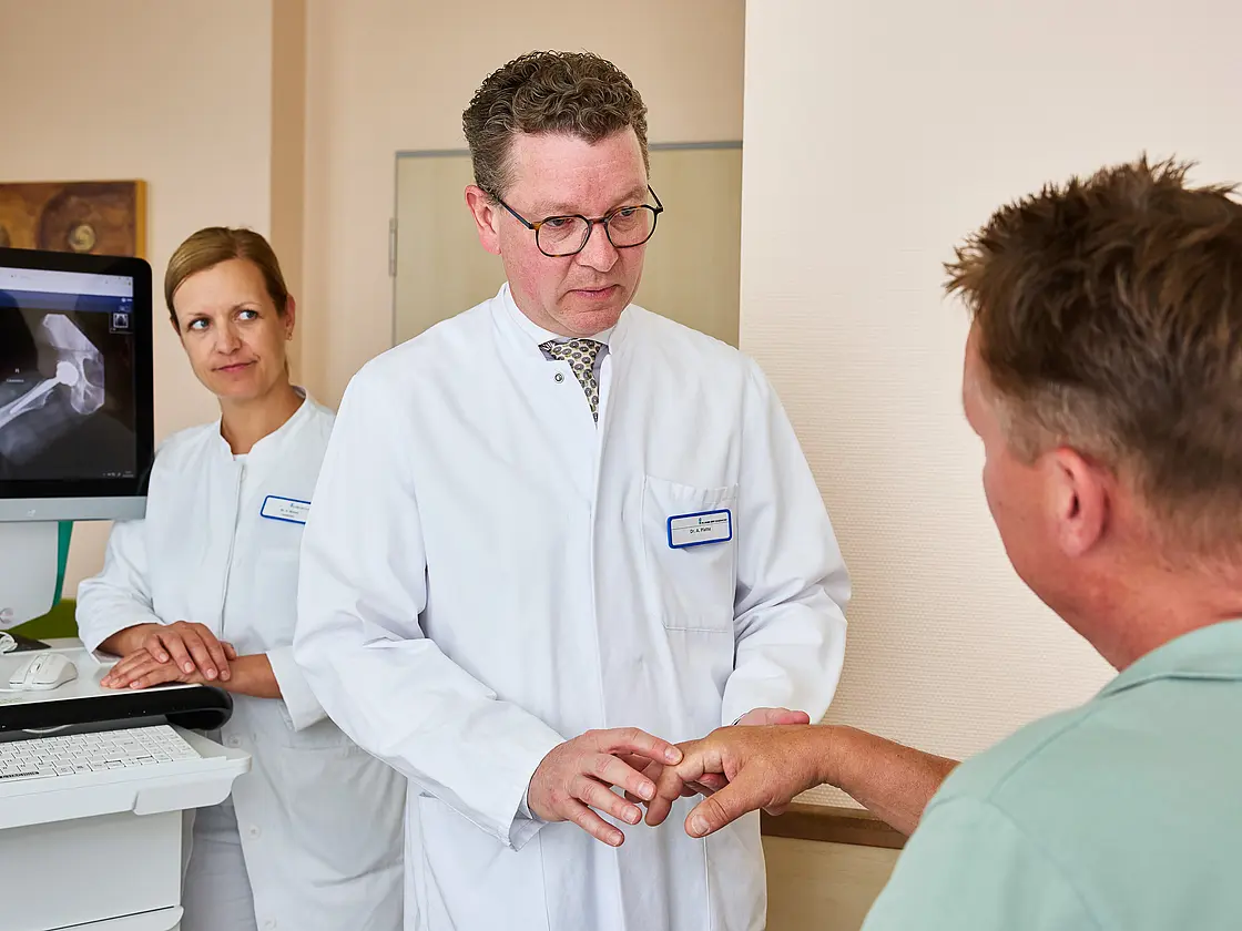 Dr. med. Ansgar Platte hält die Hand eines sitzenden Patienten und überprüft gezielt die Beweglichkeit einzelner Finger.