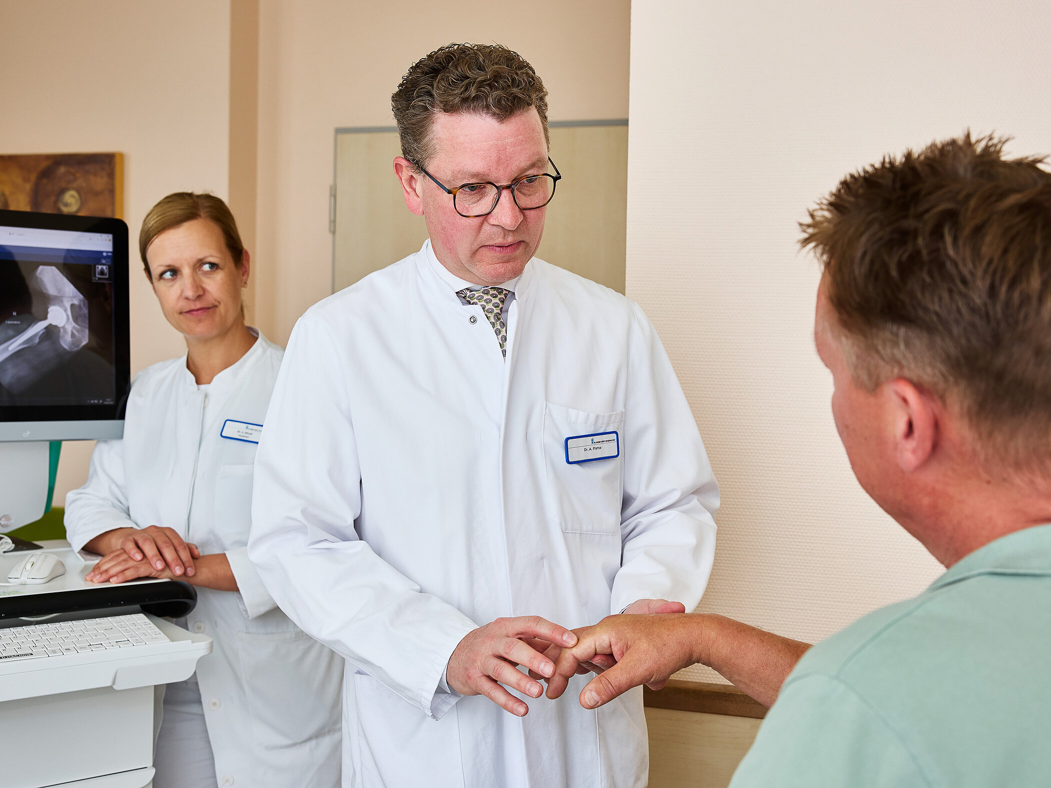 Dr. med. Ansgar Platte hält die Hand eines sitzenden Patienten und überprüft gezielt die Beweglichkeit einzelner Finger.