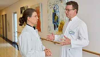 Dr. med. Ansgar Platte spricht mit einem Mitarbeiter im Flur der Klinik; beide stehen sich zugewandt gegenüber.