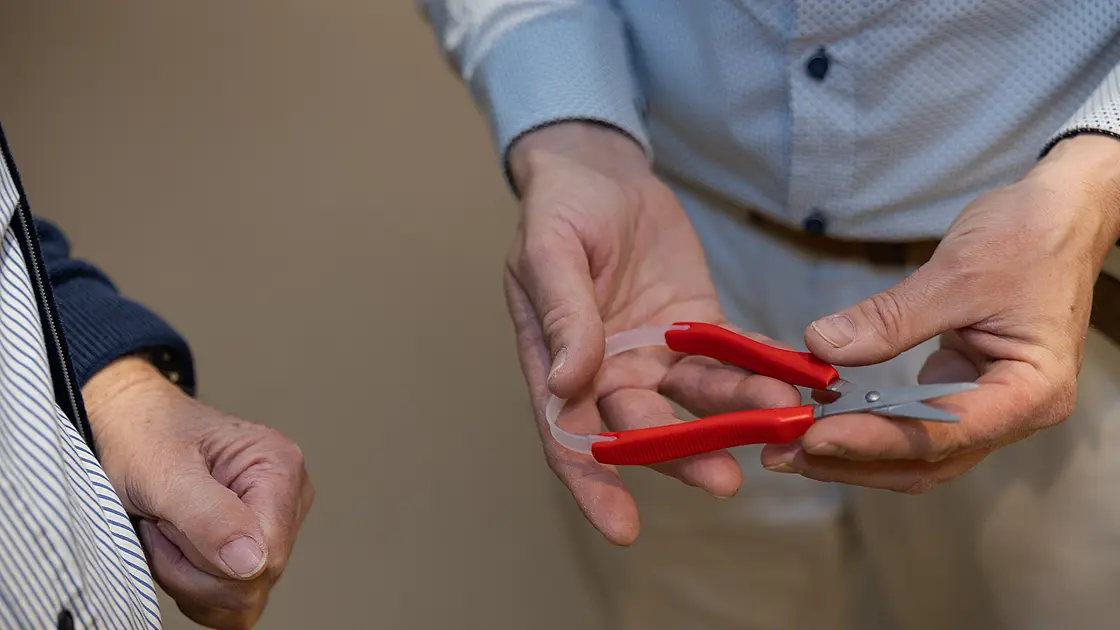 Zwei Personen betrachten gemeinsam eine kleine rote Schere, die zur Handhabung demonstriert wird.