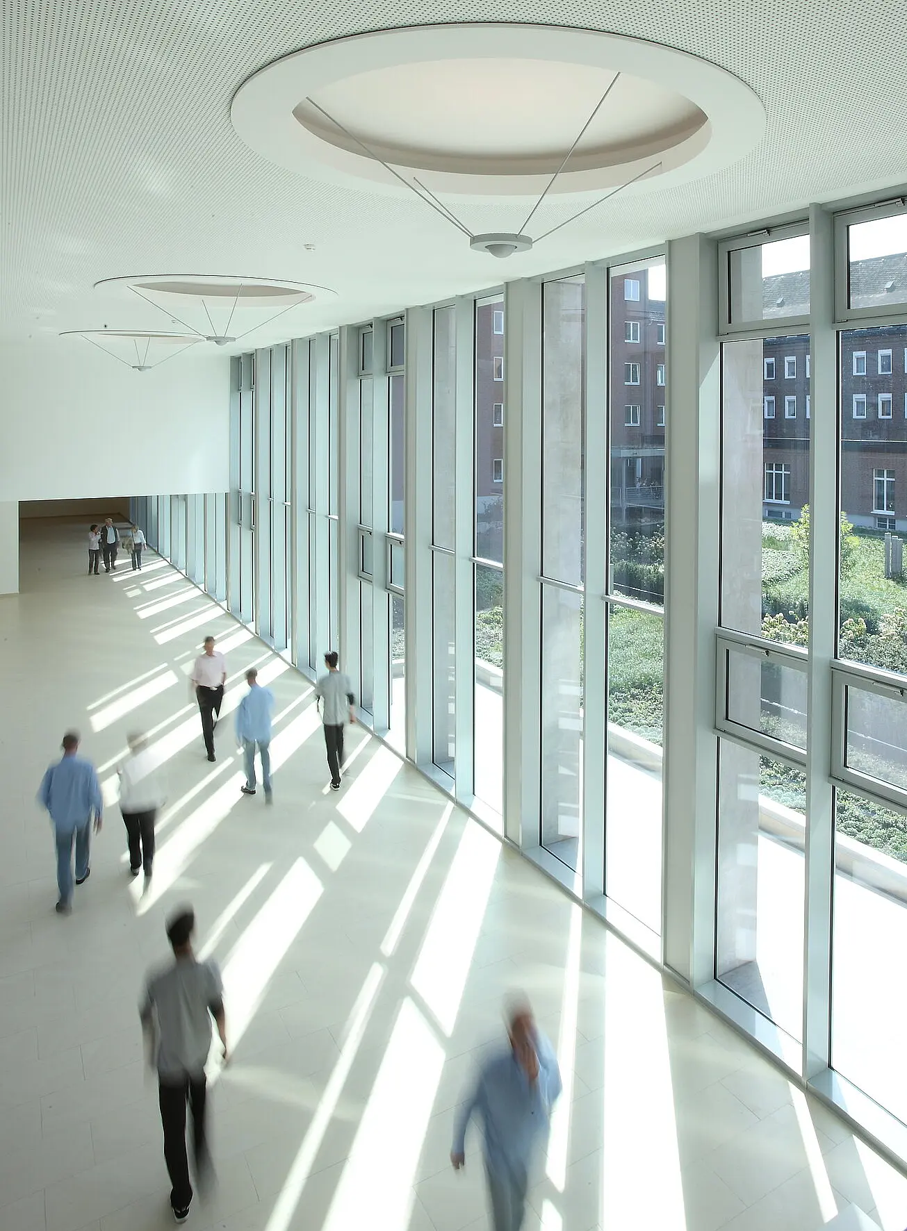 Blick auf die Magistrale des St. Josef-Stift Sendenhorst, durch die mehrere Menschen gehen und sich im öffentlichen Innenraum begegnen.