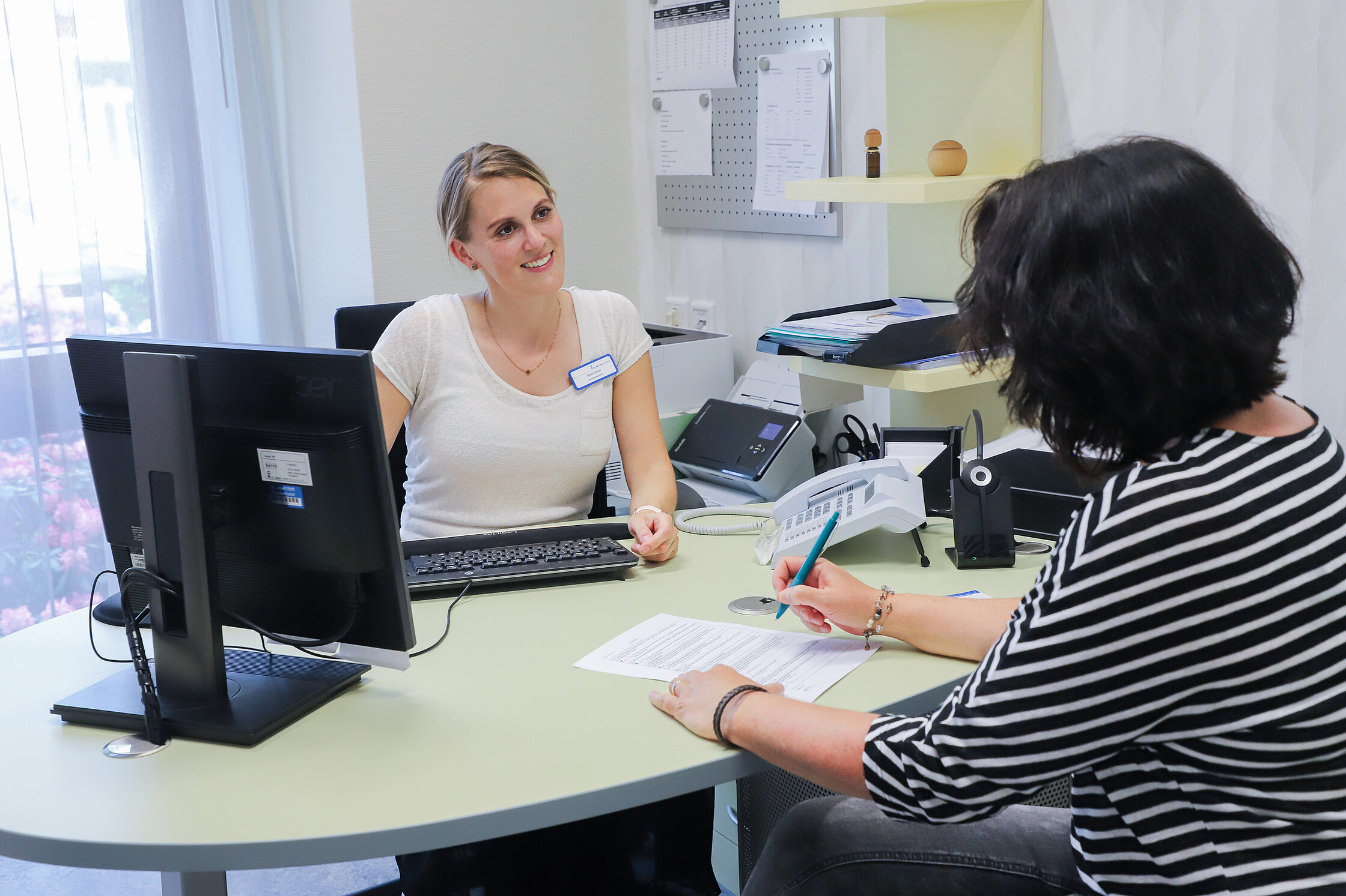 Mitarbeiterin des Sozialdienstes berät eine Patientin in ruhiger Atmosphäre an einem Schreibtisch.