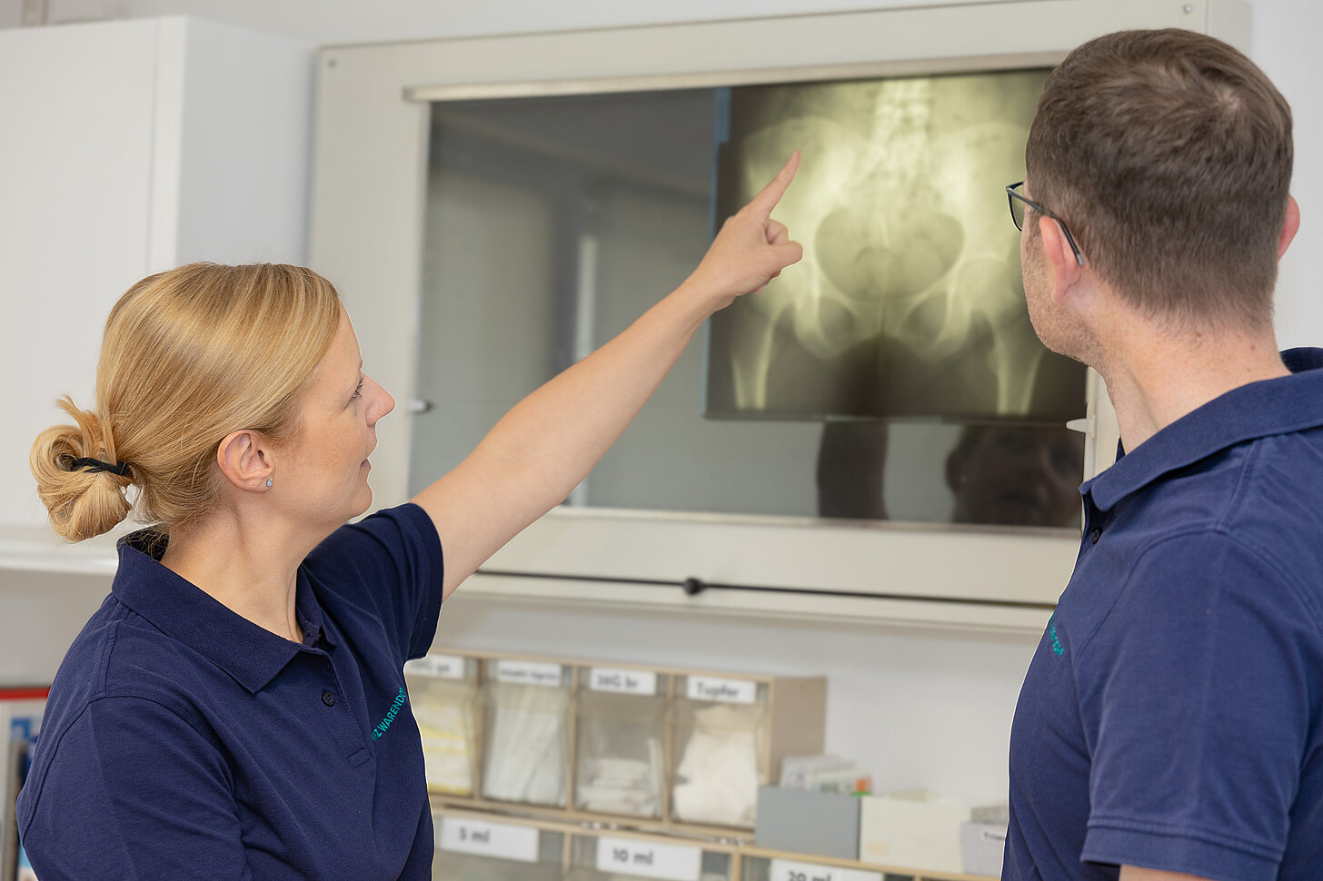 Zwei Mitarbeitende des MVZ Warendorf betrachten gemeinsam ein Röntgenbild an einer beleuchteten Wand und besprechen die Aufnahme.