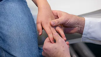 Dr. PD Daniel Windschall hält behutsam die Hand eines Kindes und untersucht die Finger.