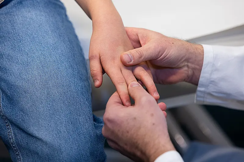 Die Hand von Dr. PD Daniel Windschall hält einen Ultraschallkopf auf dem Bauch eines liegenden Kindes während einer Untersuchung.