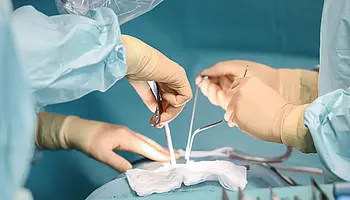 Chirurgischer Eingriff: Hände von medizinischem Personal während einer Operation am Rücken.