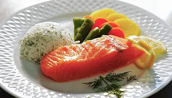 Angerichteter Teller mit Lachsfilet, Reis, Gemüse und Zitronenscheiben.