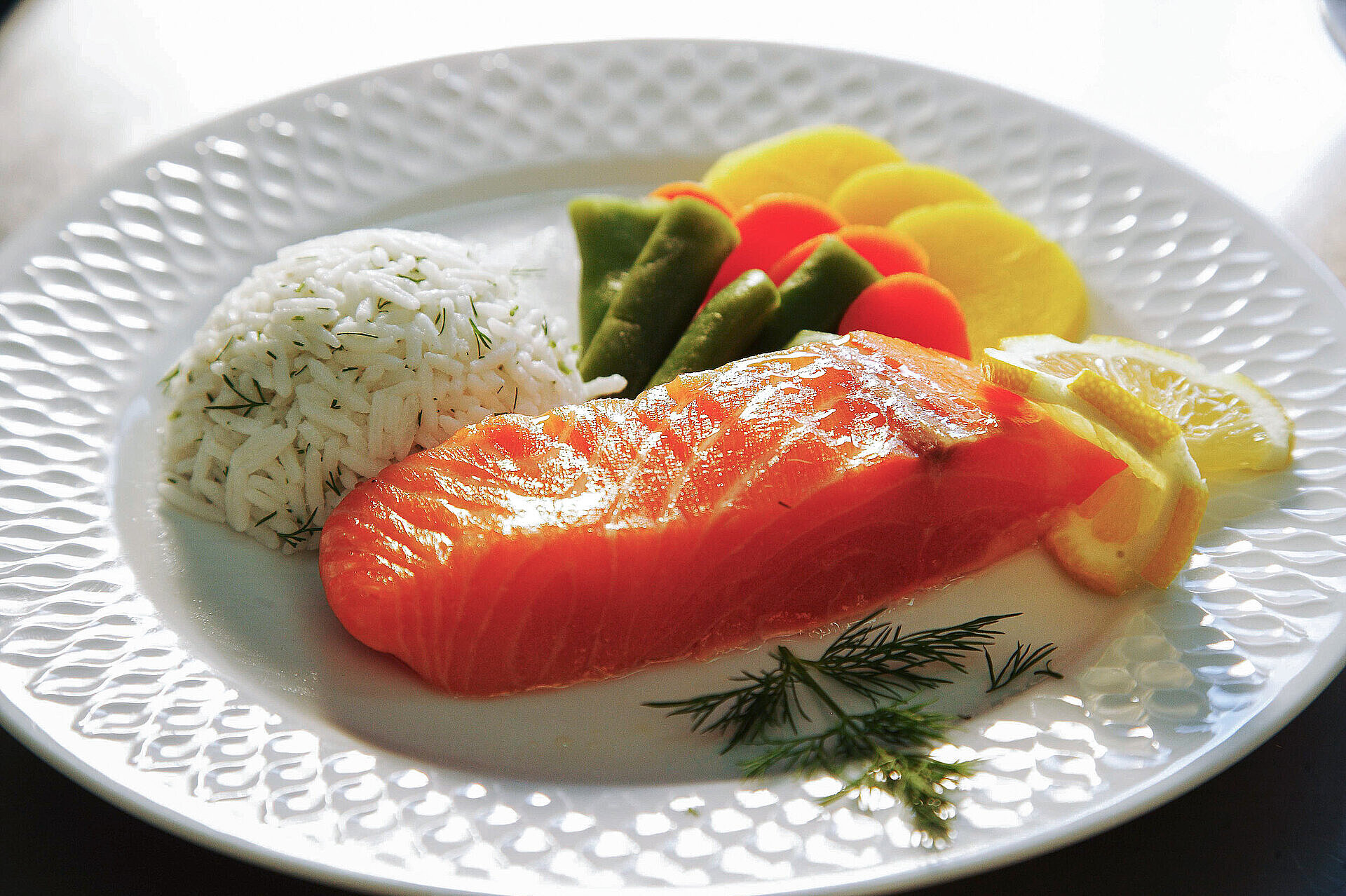 Angerichteter Teller mit Lachsfilet, Reis, Gemüse und Zitronenscheiben.