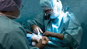 Oberärztin Shabnam Schade führt gemeinsam mit einem Teammitglied einen ambulanten chirurgischen Eingriff an einer Hand durch. Sie arbeitet hochkonzentriert mit chirurgischen Instrumenten.