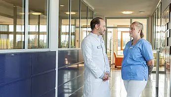 PD Dr. med. Peter Korsten spricht mit einer Kollegin in ärztlicher Kleidung auf einem hellen Klinikflur.