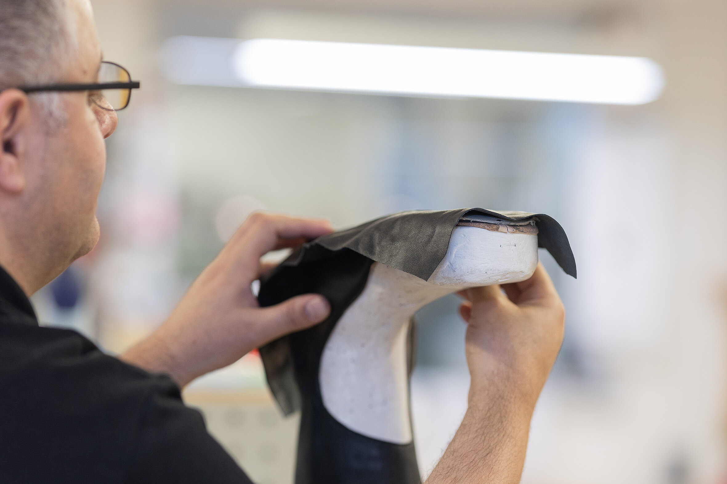 Mitarbeiter passt das Lederoberteil eines orthopädischen Schuhs an einem weißen Leisten in der Werkstatt an.