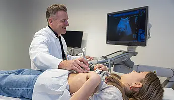 Eine Hand bedient die Tasten eines Ultraschallgeräts. Auf dem Gerät sind verschiedene Einstellknöpfe und Bedienelemente zu sehen.