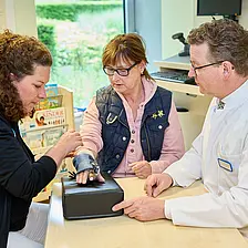 Eine Ergotherapeutin justiert eine Handorthese am Unterarm einer Patientin, während Dr. med. Ansgar Platte den Vorgang begleitet.