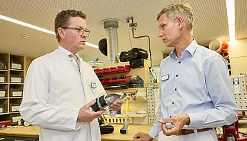 Dr. med. Ansgar Platte hält ein orthopädietechnisches Bauteil in den Händen und bespricht Details mit einem Mitarbeiter der Werkstatt.