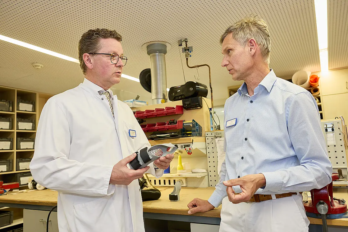 Dr. med. Ansgar Platte hält ein orthopädietechnisches Bauteil in den Händen und bespricht Details mit einem Mitarbeiter der Werkstatt.
