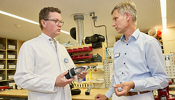 Dr. med. Ansgar Platte hält ein orthopädietechnisches Bauteil in den Händen und bespricht Details mit einem Mitarbeiter der Werkstatt.
