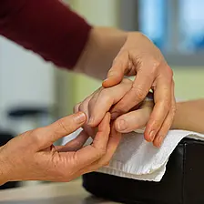 Eine Therapeutin mobilisiert vorsichtig die Finger einer auf einem Kissen gelagerten Hand.