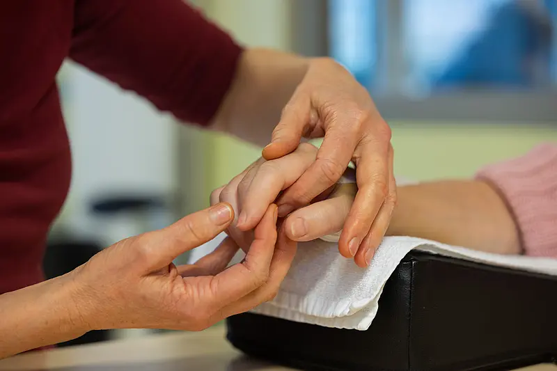 Eine Therapeutin mobilisiert vorsichtig die Finger einer auf einem Kissen gelagerten Hand.