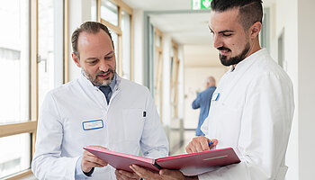 PD Dr. med. Peter Korsten und ein Kollege betrachten gemeinsam eine geöffnete Aktenmappe auf einem Klinikflur.