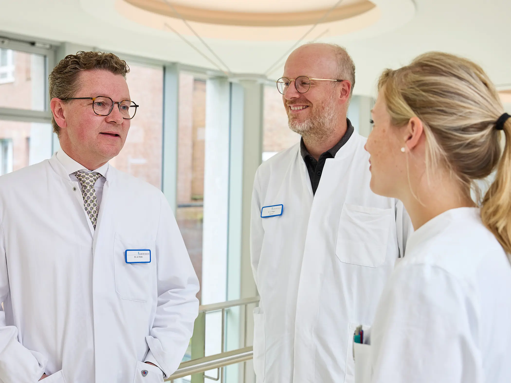 Dr. med. Ansgar Platte spricht im hellen Klinikflur mit zwei Mitarbeitenden in medizinischer Arbeitskleidung.