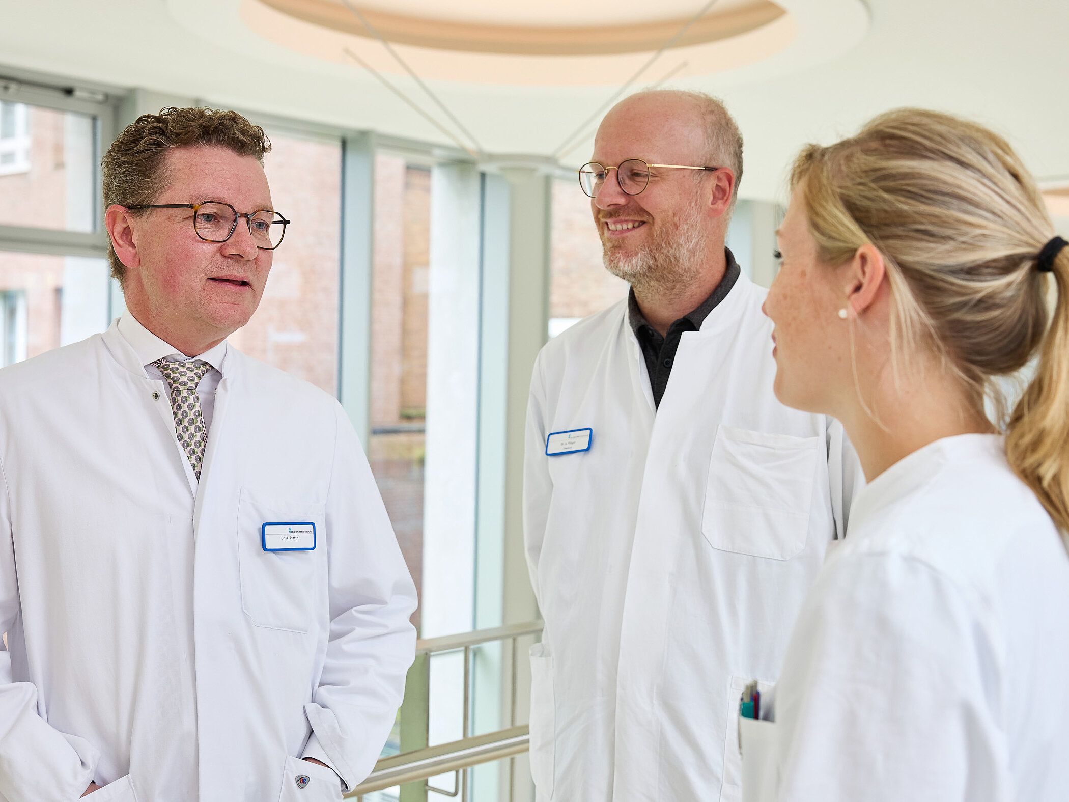 Dr. med. Ansgar Platte spricht im hellen Klinikflur mit zwei Mitarbeitenden in medizinischer Arbeitskleidung.