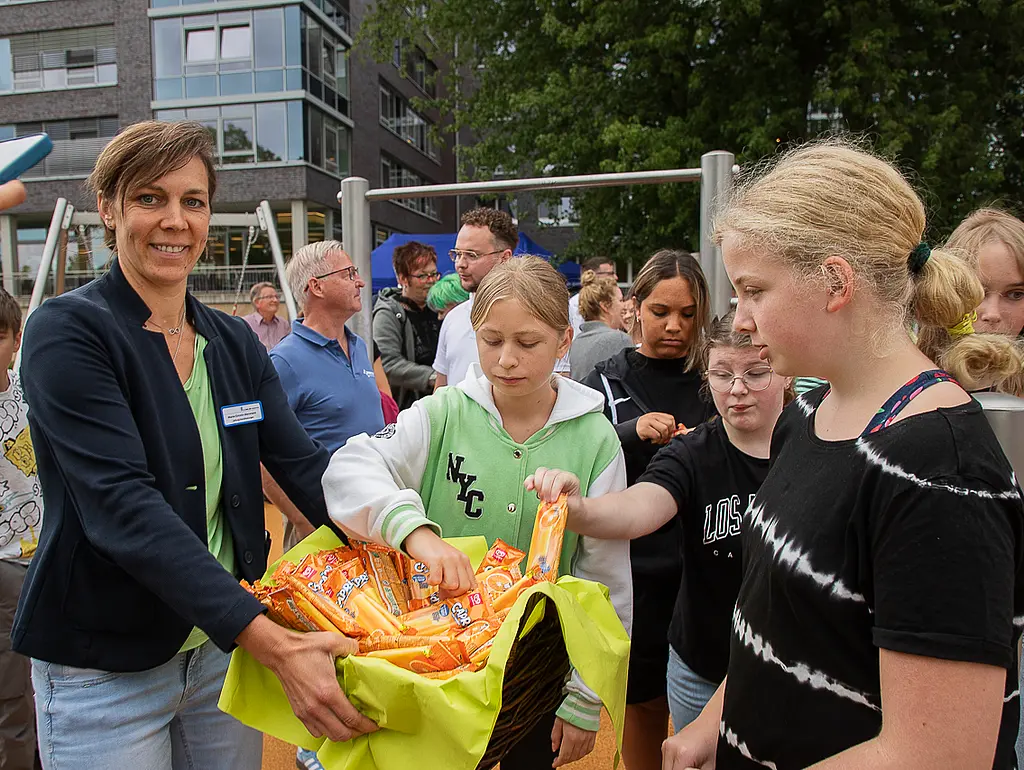 Eine Frau hält Kindern einen Korb mit Eis hin, die Kinder greifen erfreut in den Korb.