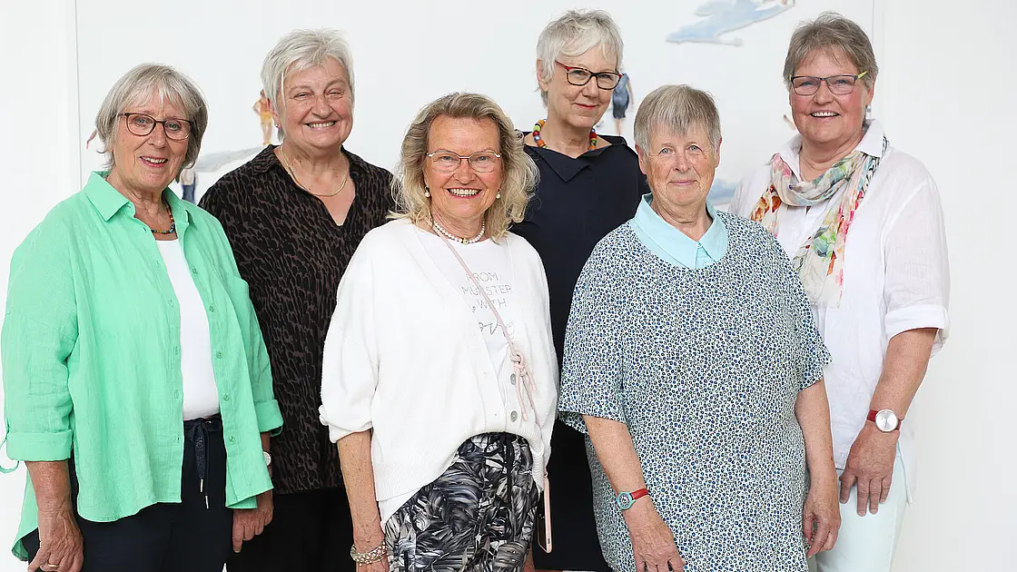 Mehrere Personen stehen als Gruppe in einem hellen Innenraum.