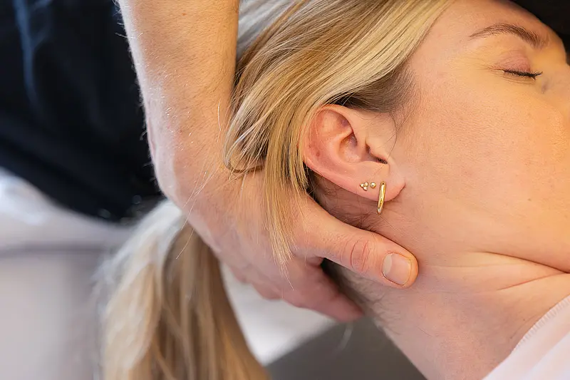 Die Hände eines Physiotherapeuten massieren den Nacken einer Patientin.