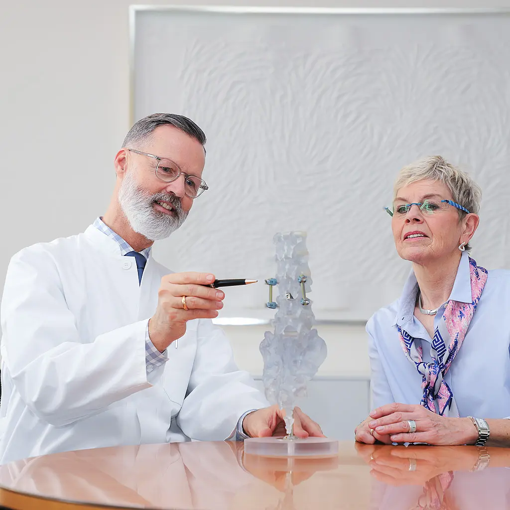 Chefarzt Dr. Brinkmann erklärt einer Patientin anhand eines transparenten Wirbelsäulenmodells den Aufbau der Wirbelsäule und das Vorgehen während der OP.
