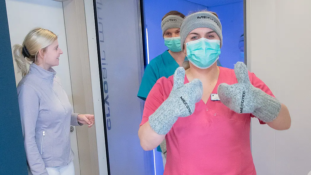 Mitarbeitende mit Mundschutz und Kälteschutzhandschuhen treten aus einer geöffneten Kältekammer; kalter Dampf ist im Raum sichtbar.