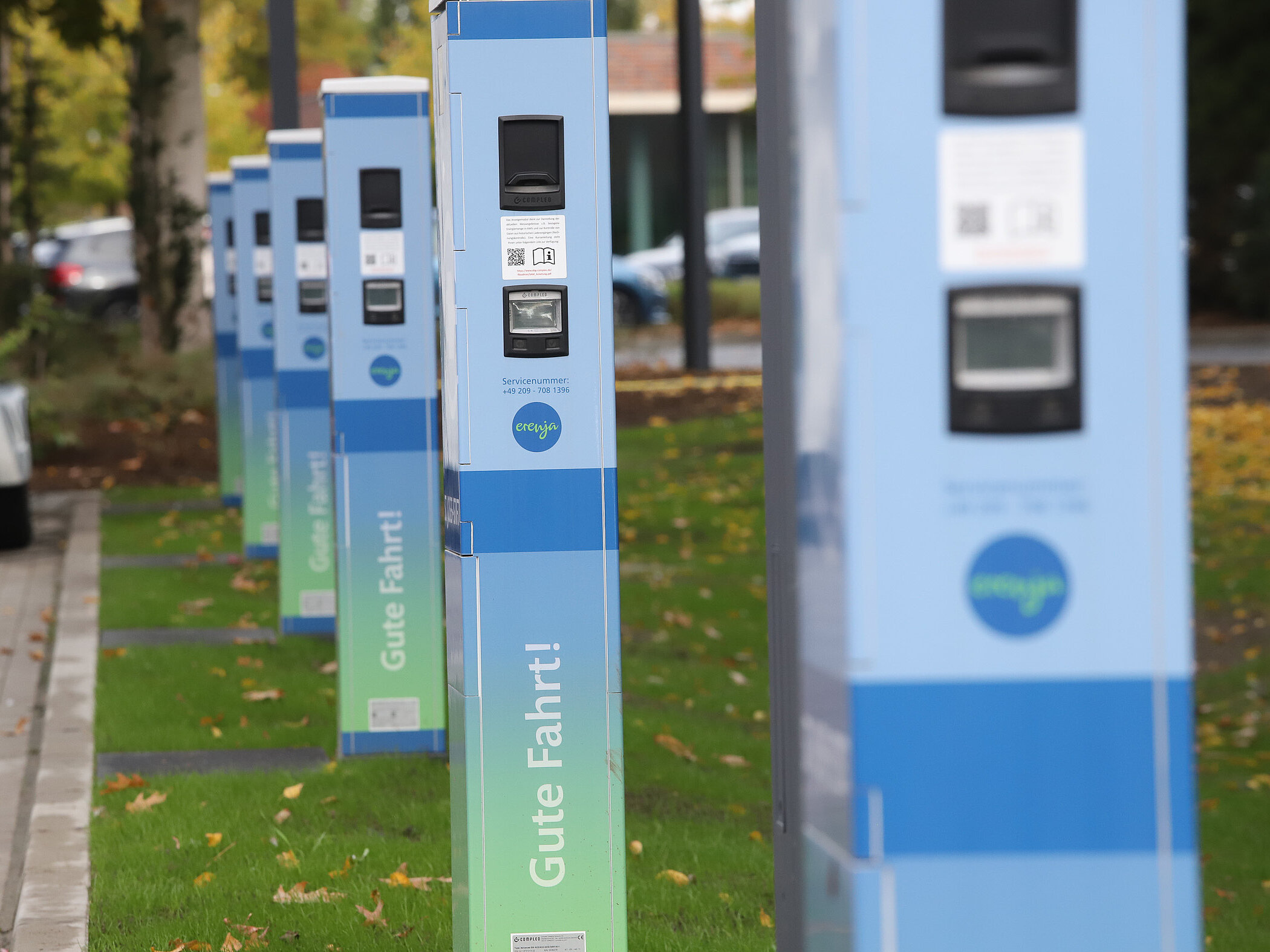 Großer Parkplatz mit abgestellten Fahrzeugen, im Hintergrund herbstlich gefärbte Bäume und Gebäude des Klinikgeländes.