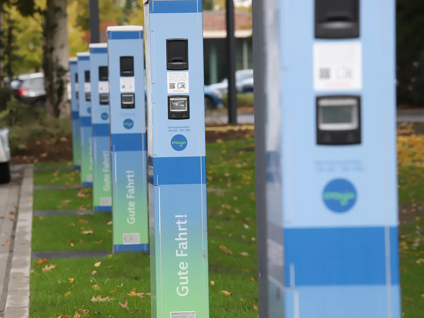 Großer Parkplatz mit abgestellten Fahrzeugen, im Hintergrund herbstlich gefärbte Bäume und Gebäude des Klinikgeländes.