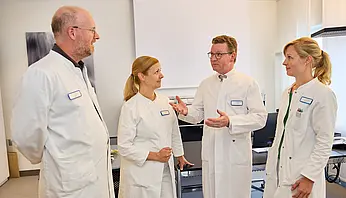 Dr. med. Ansgar Platte steht im Gespräch mit drei Mitarbeitenden in einem Behandlungsraum.