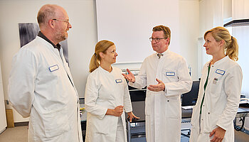 Dr. med. Ansgar Platte steht im Gespräch mit drei Mitarbeitenden in einem Behandlungsraum.