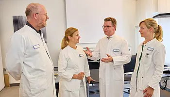 Dr. med. Ansgar Platte steht im Gespräch mit drei Mitarbeitenden in einem Behandlungsraum.