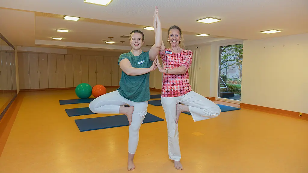Zwei Yoga-Lehrerinnen stehen in einem Trainingsraum und zeigen eine gemeinsame Yoga-Position.