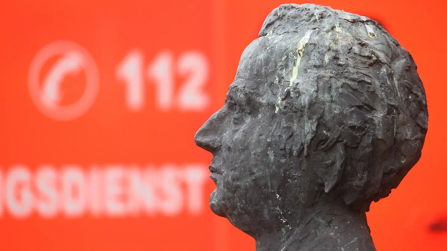 Skulptur vor dem St. Josef-Stift im Vordergrund. Im Hintergrund ist ein Notarztwagen zu sehen.